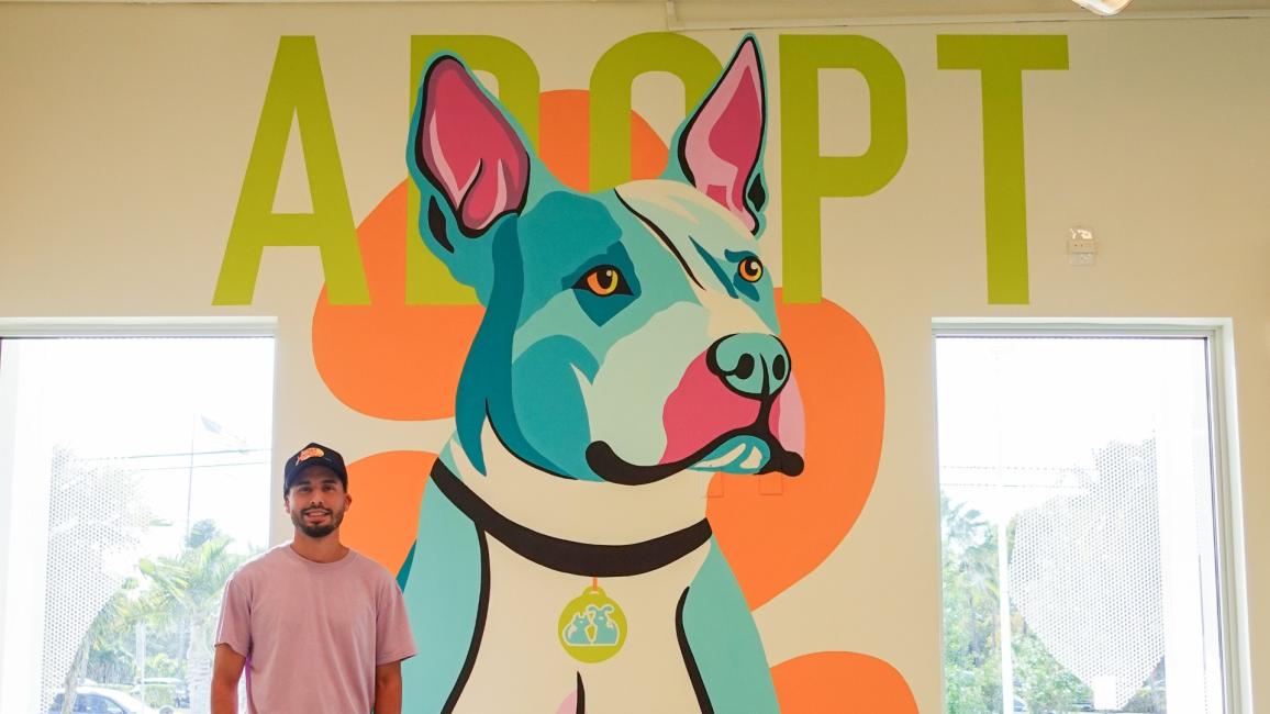 Jonathan Ramirez next to his mural of a dog with the word, Adopt